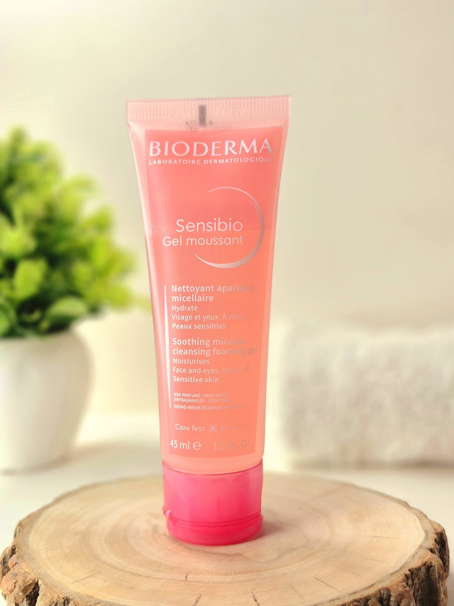 Bioderma Sensibio Gel Moussant in a pink tube on a light wooden surface with plants.