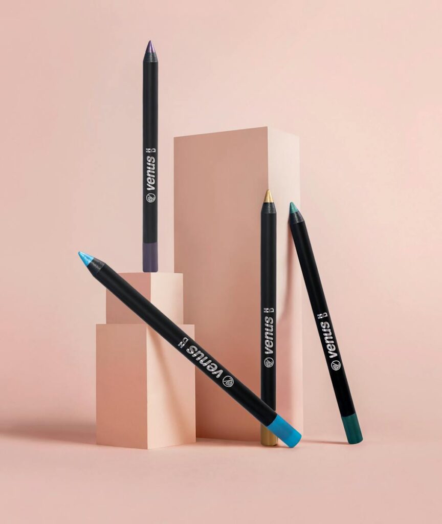 A creative arrangement of colorful eyeliners on a pink background, perfect for showcasing beauty products.