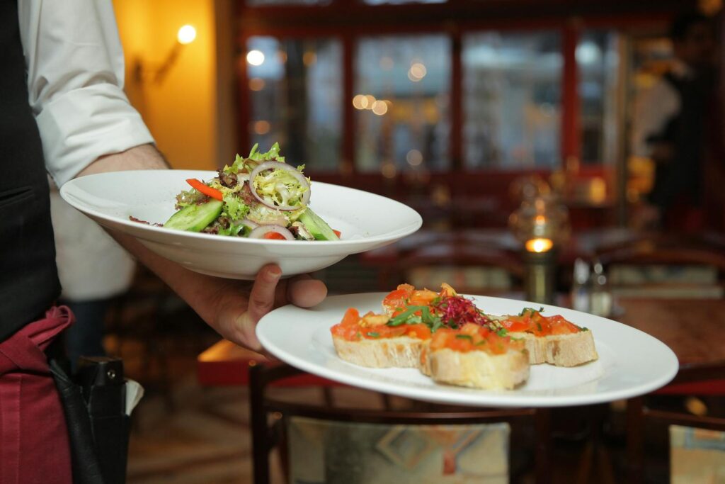 A waiter serves a fresh salad and hors d'oeuvres in a cozy restaurant setting.