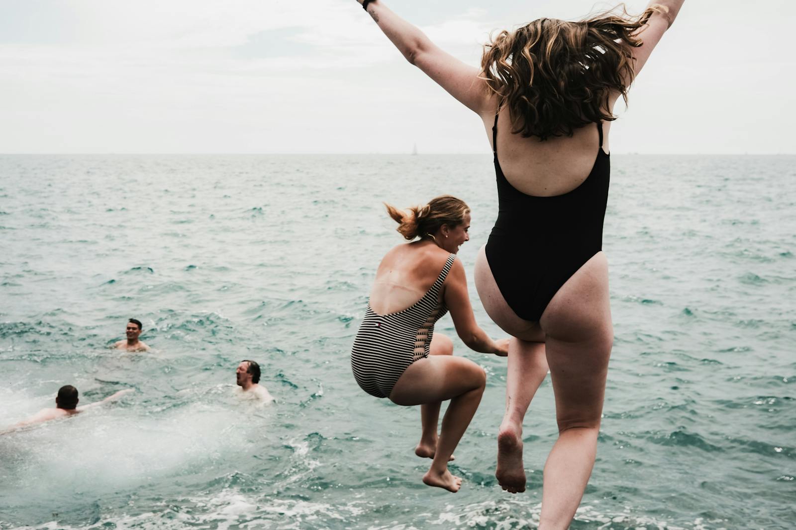 Friends enjoy a summer day by jumping into Lake Michigan, embodying fun and freedom.