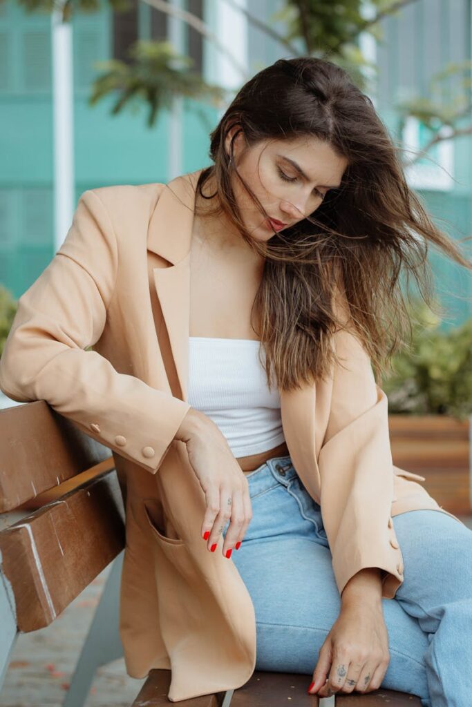 Elegant woman in a beige blazer and denim enjoying a moment on a park bench.