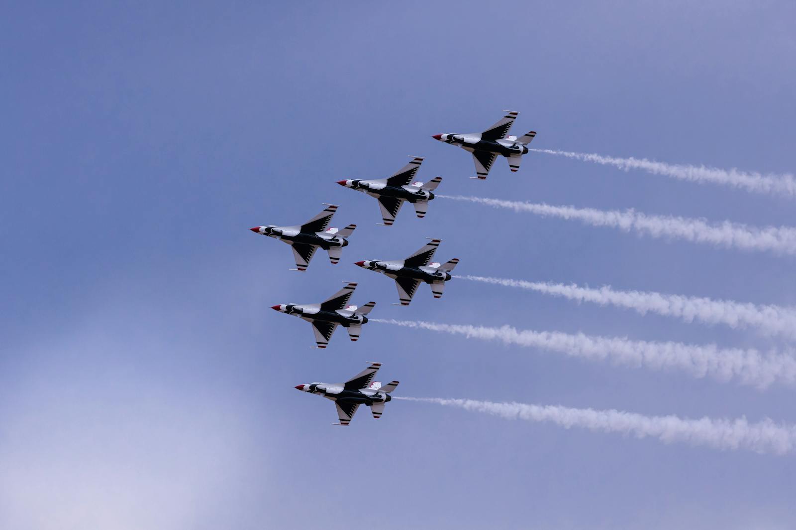 Military jets perform aerobatic maneuvers, leaving trails against a bright blue sky.