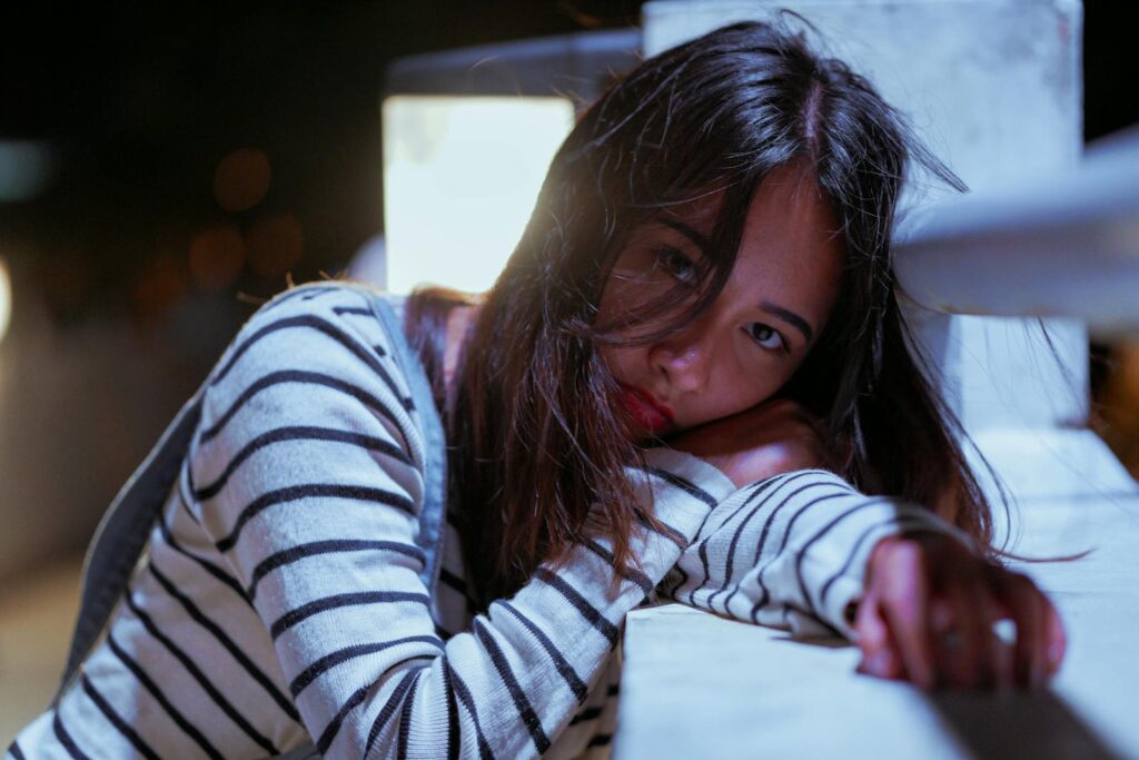 A woman in a striped sweater poses contemplatively at night in a soft focus setting.