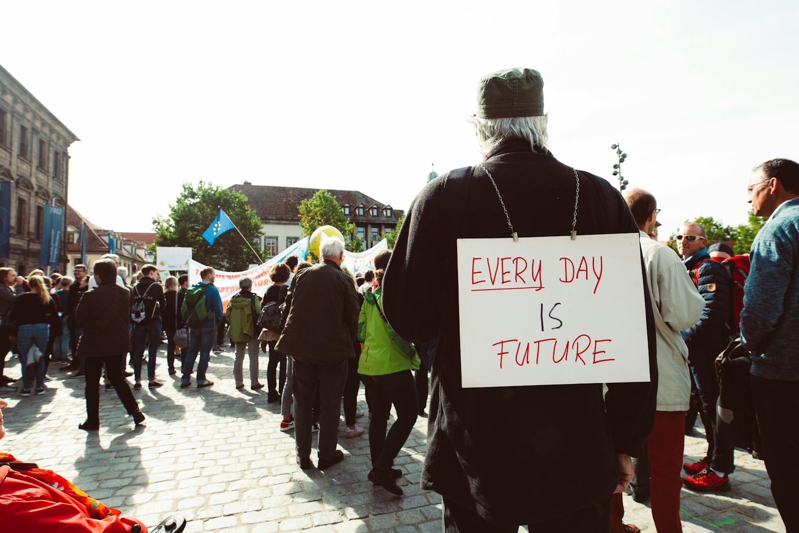 Participants at a climate rally gather on a cobblestone street with signs advocating for the future.