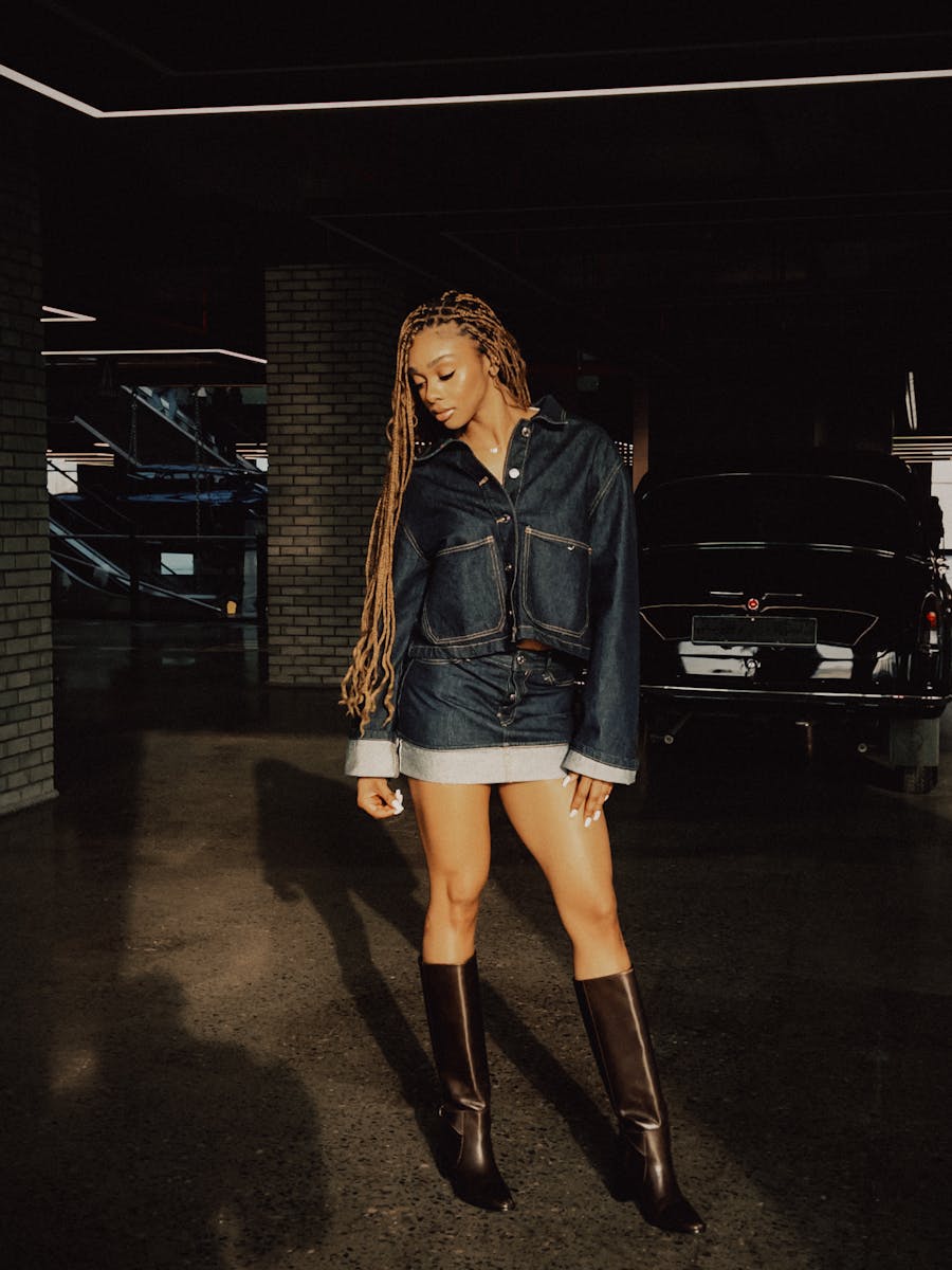 A fashionable woman in denim posing near a classic car with urban backdrop in Baku, Azerbaijan.