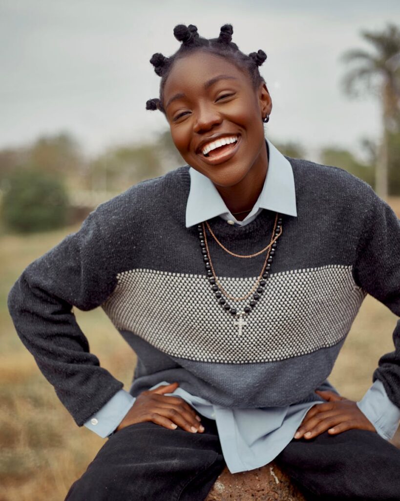 Young woman wearing sweater laughs joyfully in a natural setting.