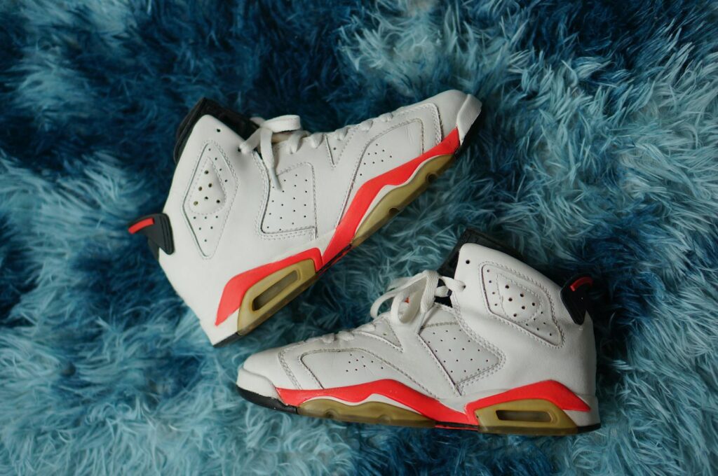 Pair of white sneakers with red accents on a textured blue furry carpet.