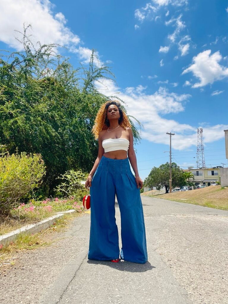 Trendy woman posing confidently in a summer street scene wearing wide-leg jeans and a crop top.