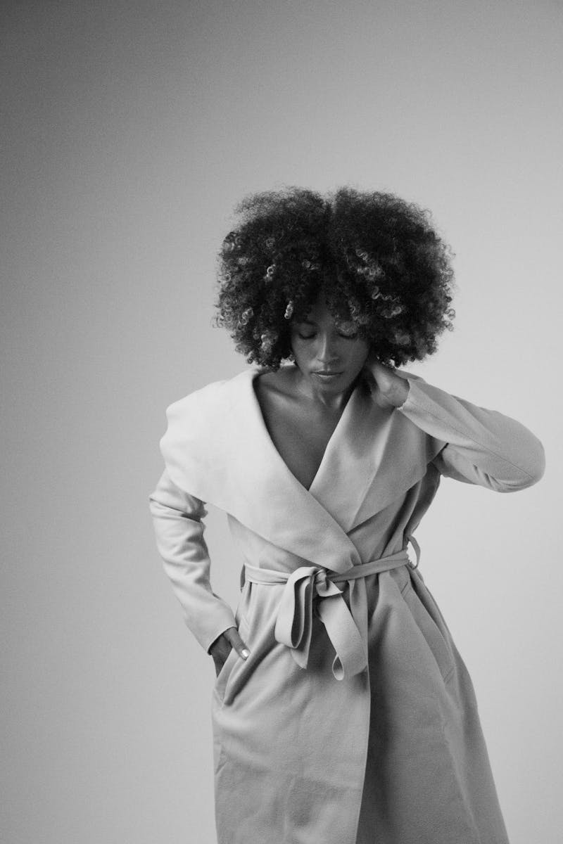 Black and white portrait of a woman with afro hair wearing a trench coat. Stylish and elegant fashion photography.