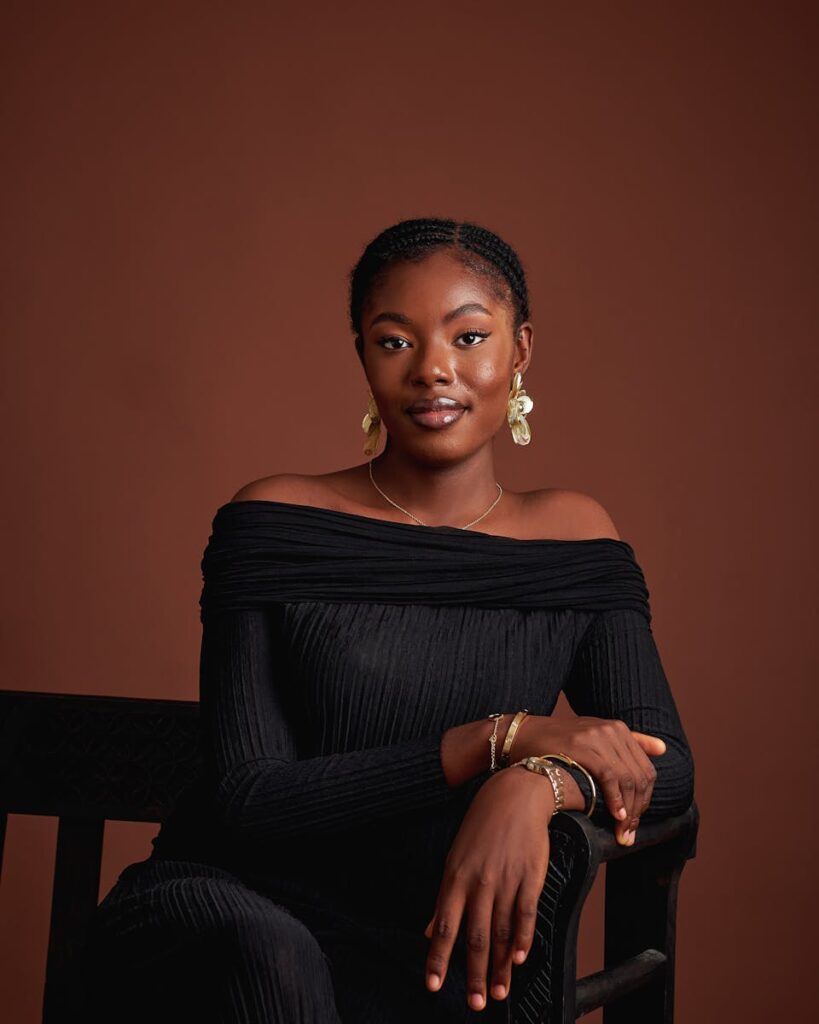 Elegant portrait of a woman in a black dress with golden earrings against a brown background.