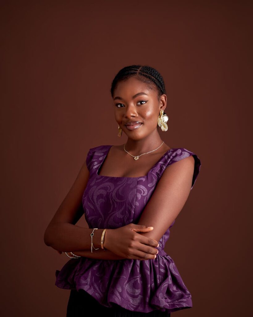 Portrait of a smiling woman in a purple dress with elegant jewelry against a brown background.