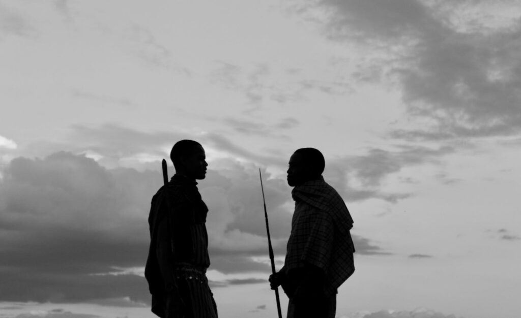 Two tribal members engaging in conversation silhouetted against the sky at sunset.