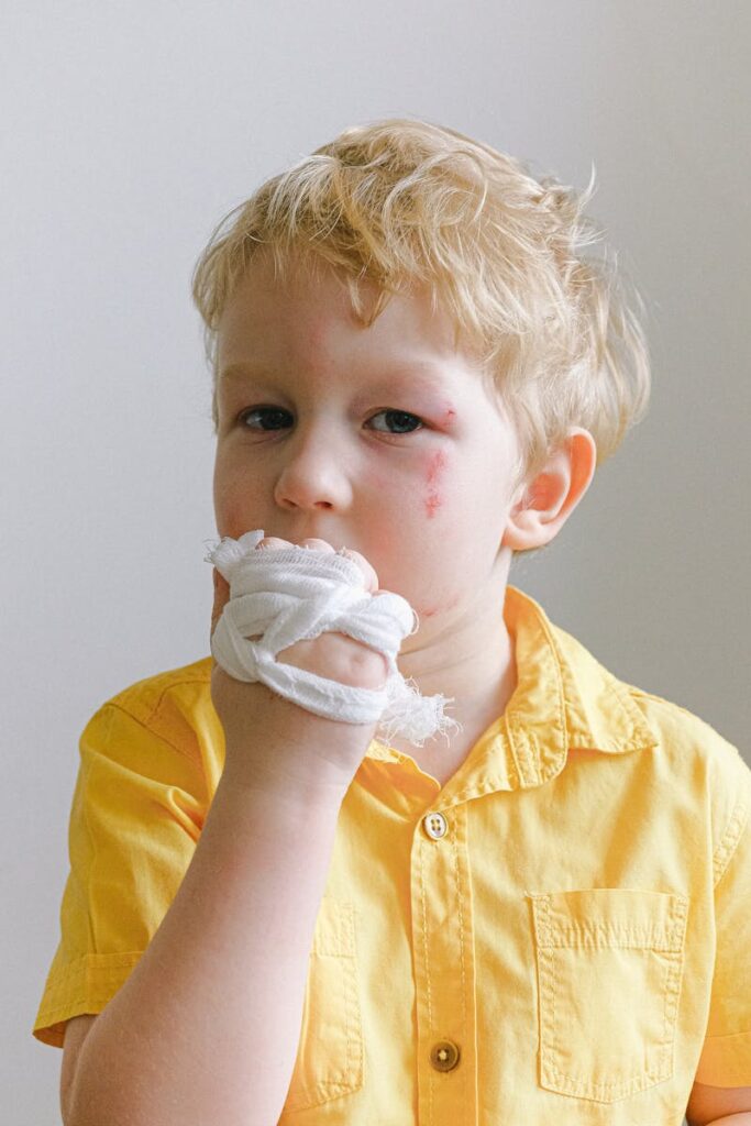 Portrait of a young boy with bandaged hand and facial injuries wearing a yellow shirt.