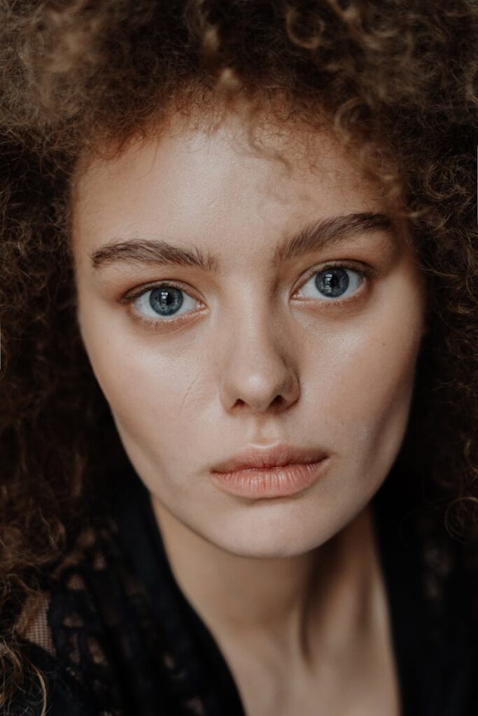 Intimate close-up portrait capturing the natural beauty of a young woman with curly hair and striking blue eyes.