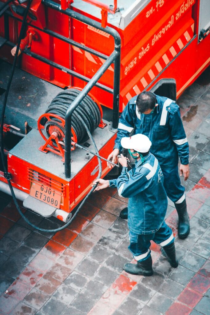 Two firefighters in uniform work with a hose on a fire truck from a high angle view.