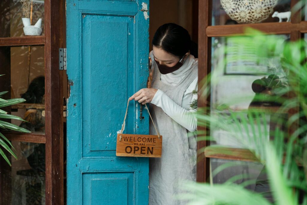 Woman opening a wooden door with an 'Open' sign, welcoming customers.