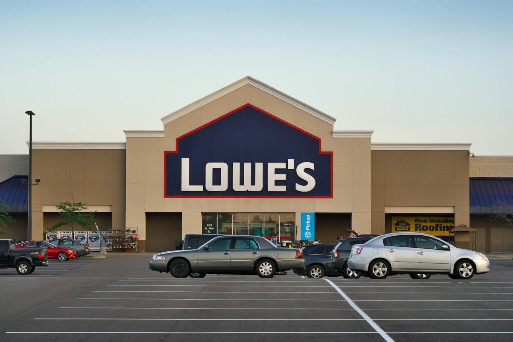 Front view of a Lowe's store entrance with parked cars in the lot during the day.