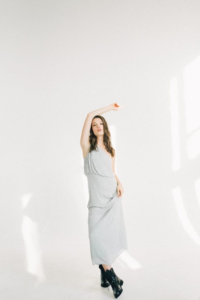 Young woman poses stylishly in a studio with natural light and a white background.