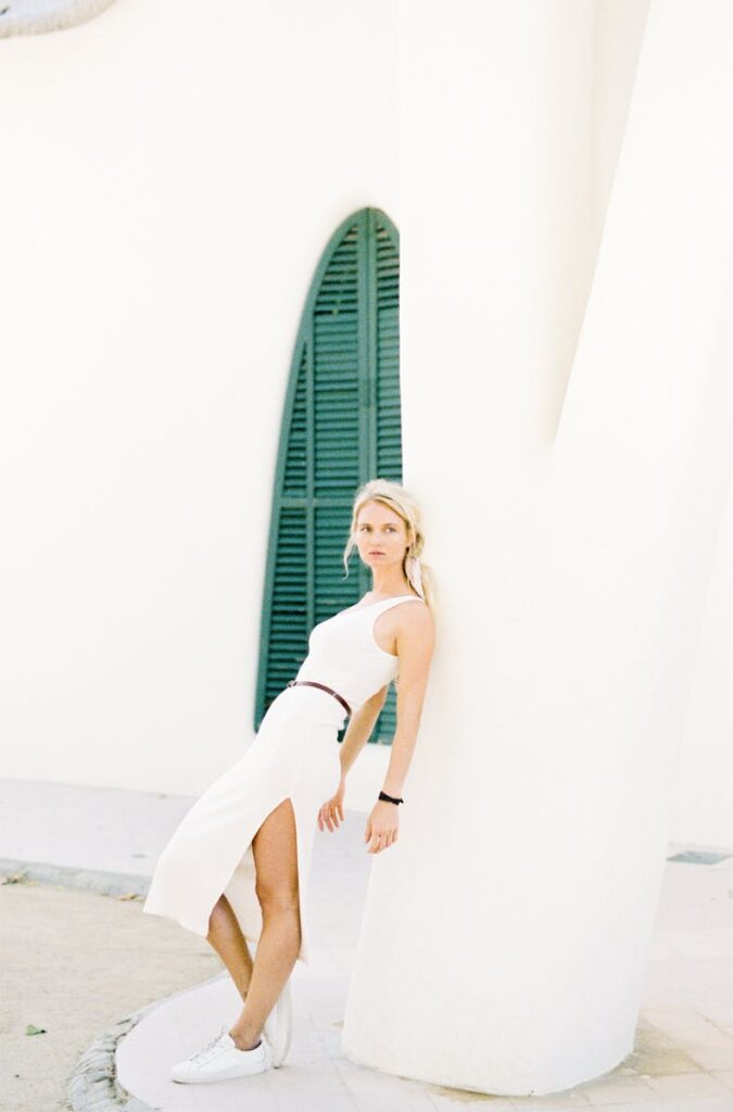 Caucasian woman in a white dress leaning against a pillar with a minimalist style.