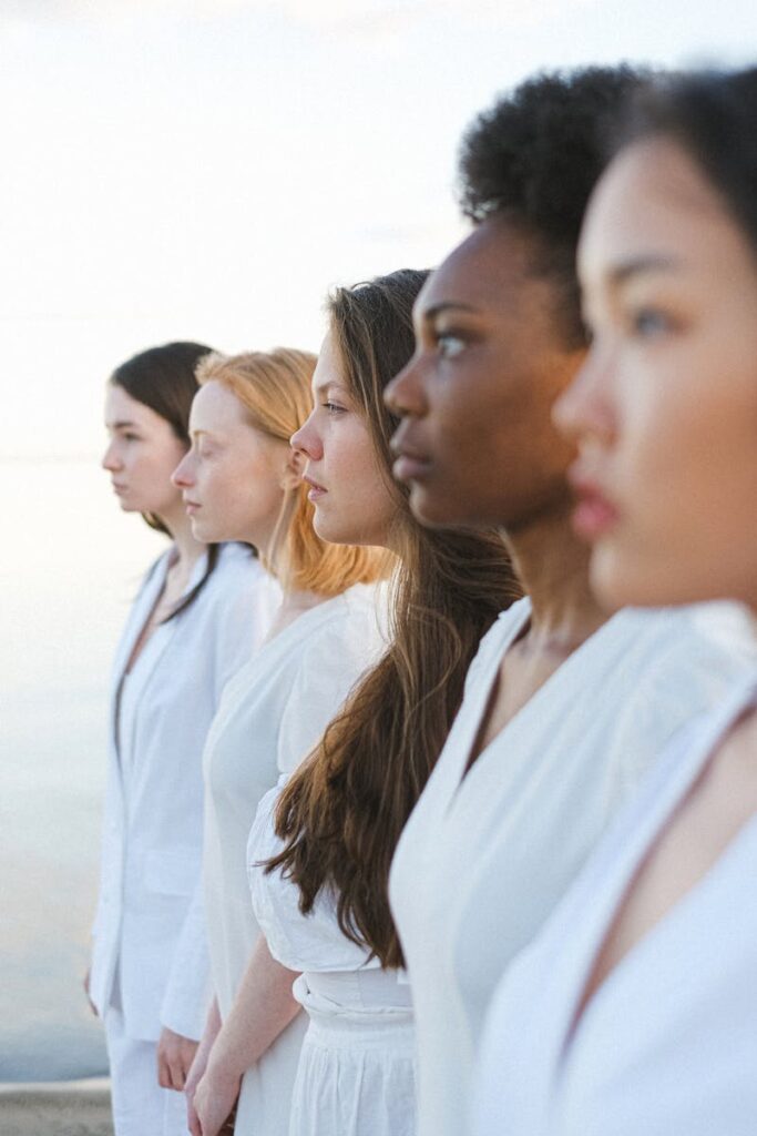 Five women of different ethnicities standing together by the sea, embracing diversity.