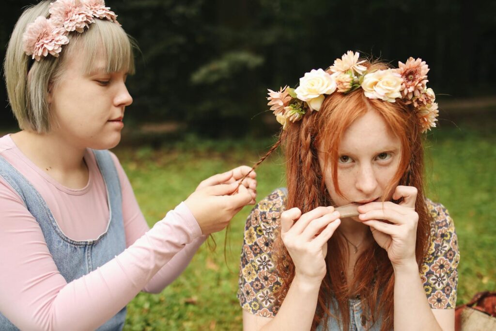 Two women with flower crowns enjoy a relaxed moment outdoors, crafting and embracing nature.