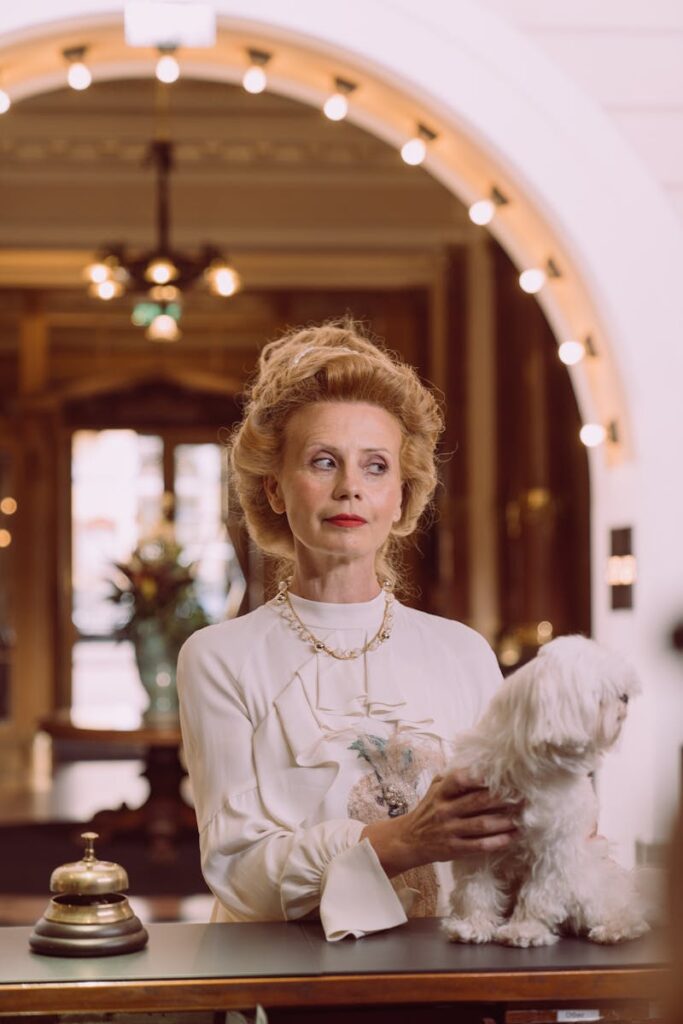 A sophisticated woman with a Maltese dog stands in a luxurious hotel lobby, exuding elegance.