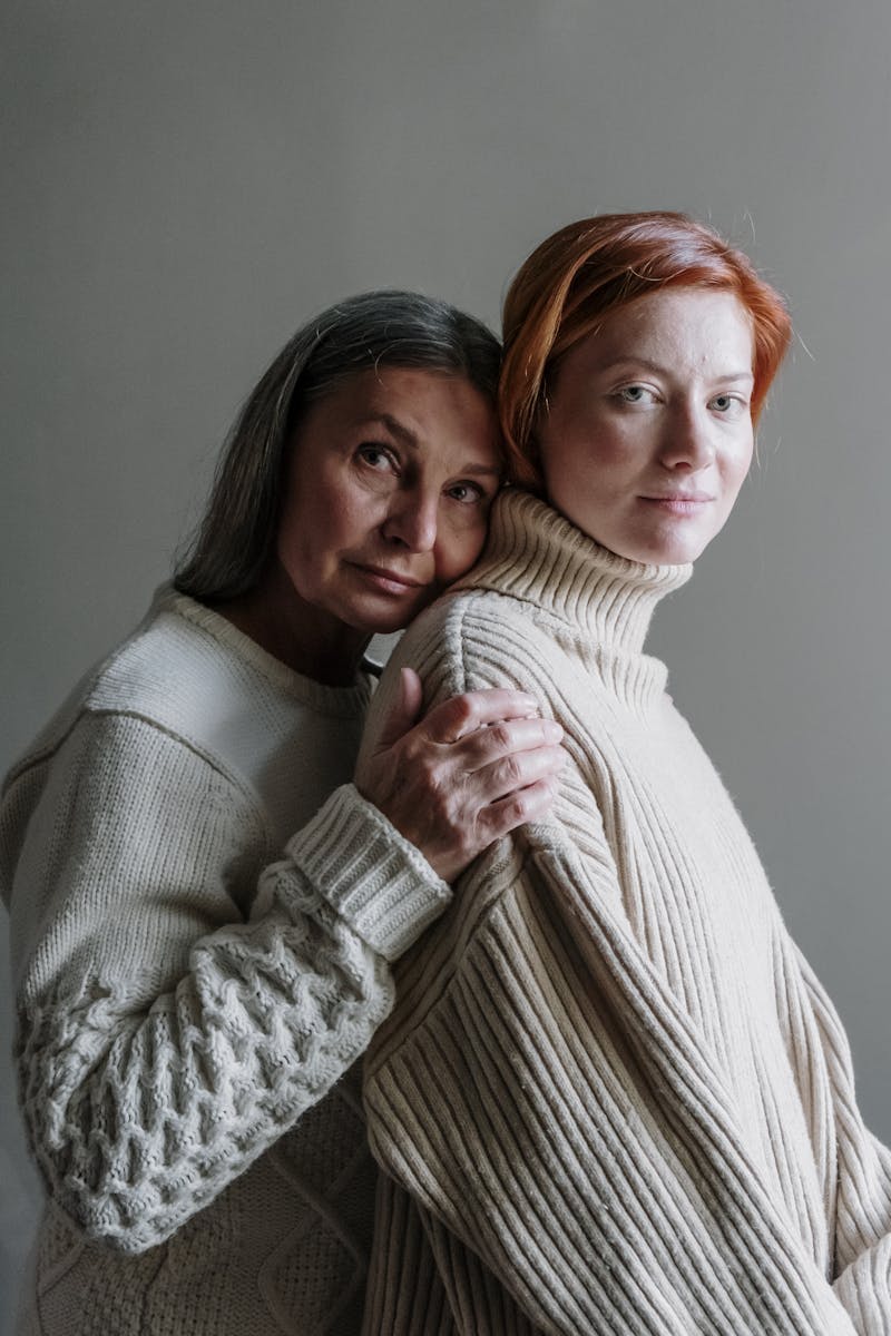 A heartwarming portrait of a mother and daughter embracing, wearing cozy knit sweaters indoors.
