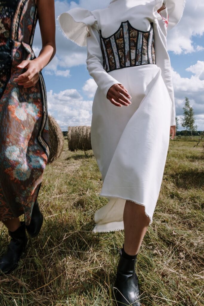 Two women in stylish dresses pose in a rustic countryside setting amidst hay bales.