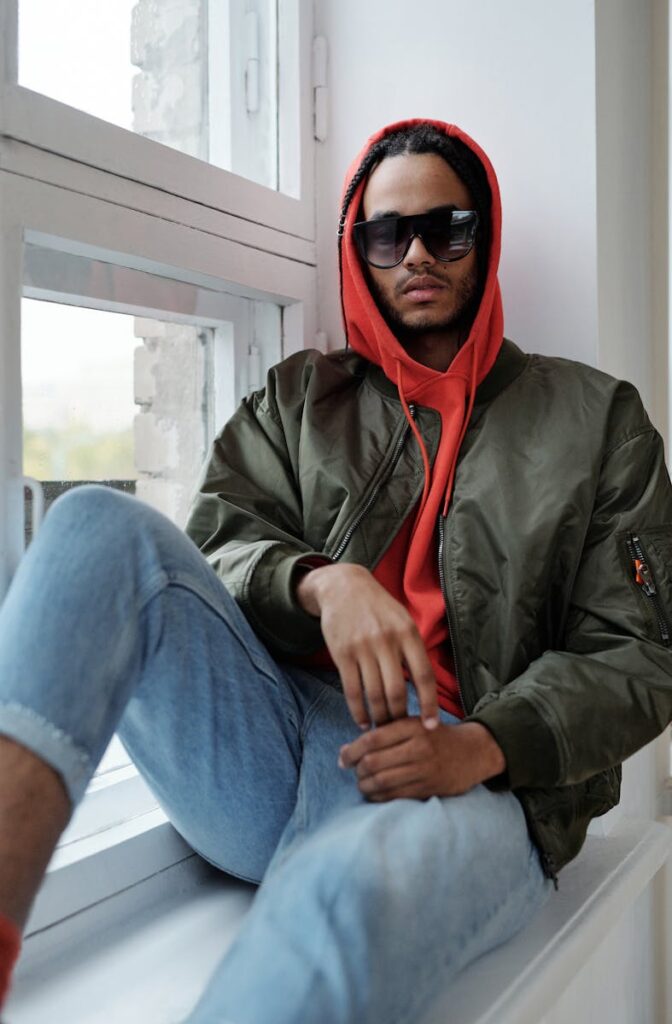 Fashionable man in streetwear sitting on a window sill, exuding urban style.