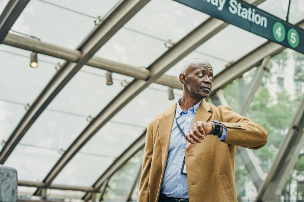 Serious African American businessman in formal clothes standing in subway station and checking time on wristwatch while looking away thoughtfully