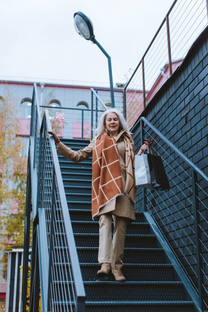 Elegant senior woman with shopping bags walking down outdoor staircase, embodying urban lifestyle.