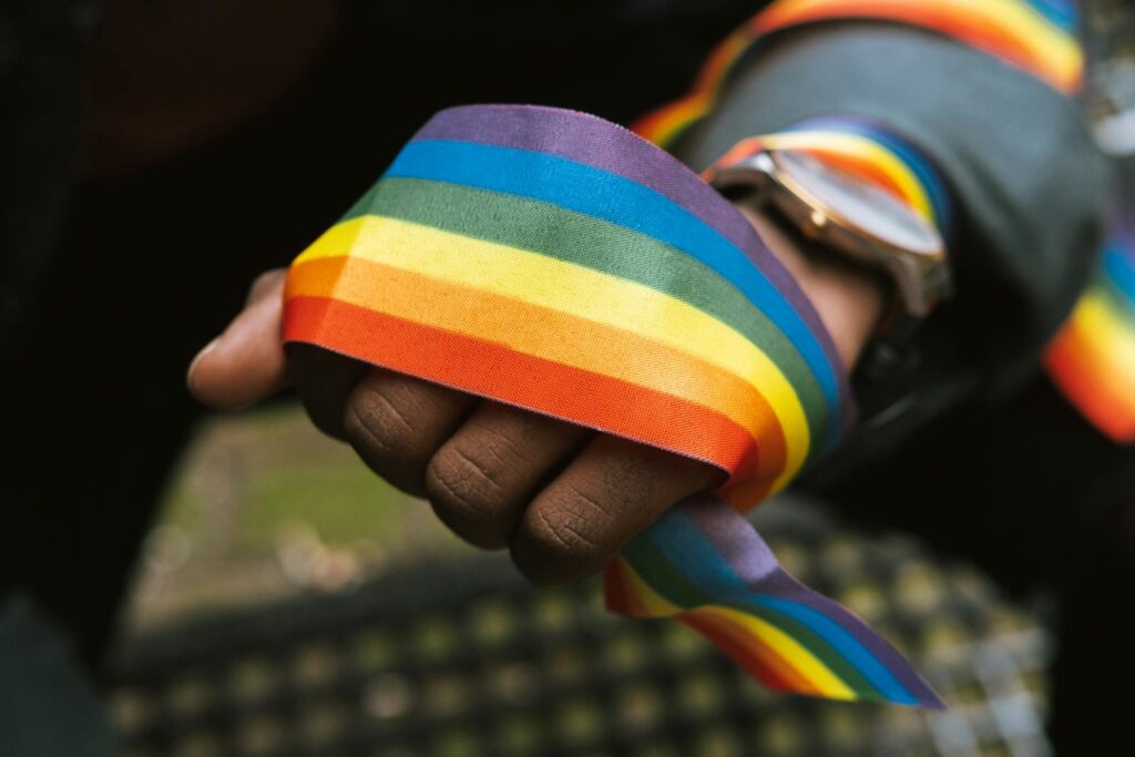 A close-up shot of a hand holding a vibrant rainbow pride ribbon, symbolizing LGBTQ pride and support.