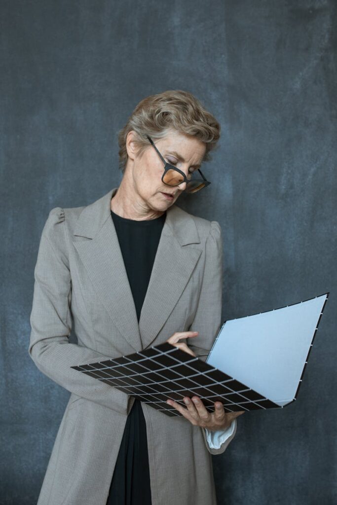 Senior woman with glasses in elegant attire examining a file folder indoors.
