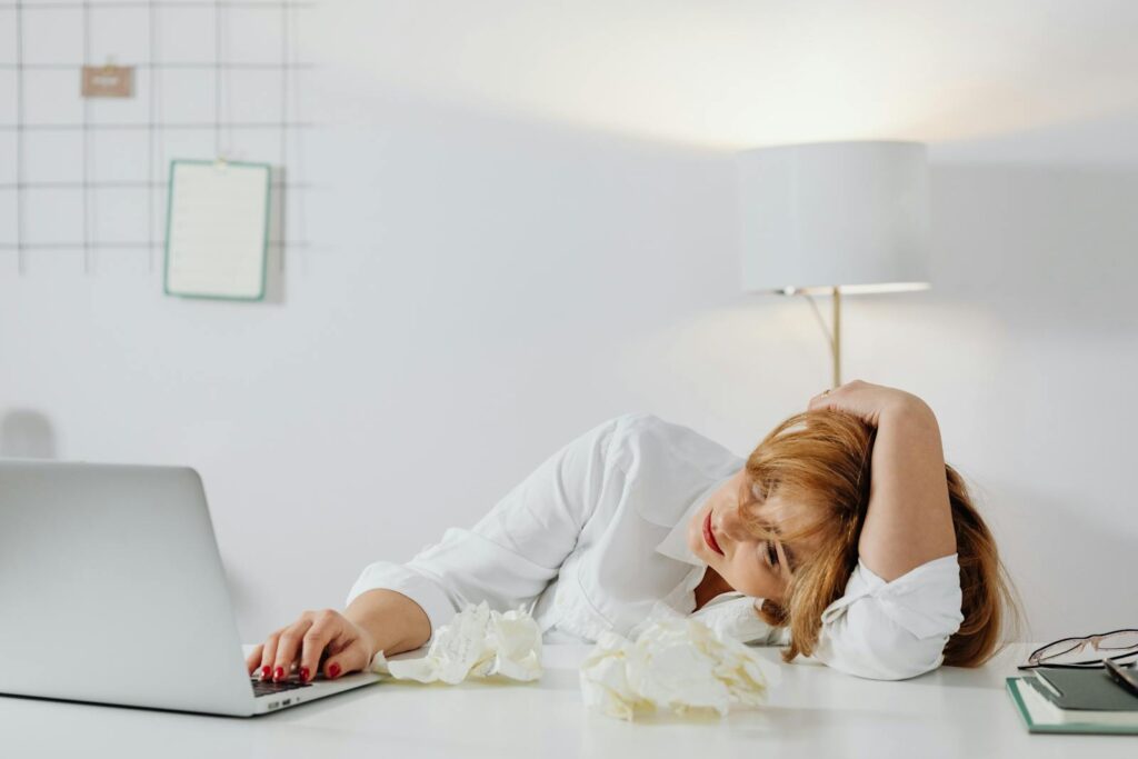 Tired woman resting head on desk with laptop, showing workplace exhaustion.