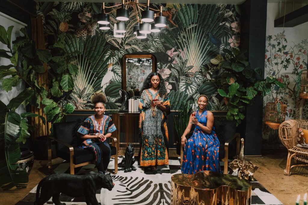 Three African women in traditional attire celebrating indoors with vibrant decor