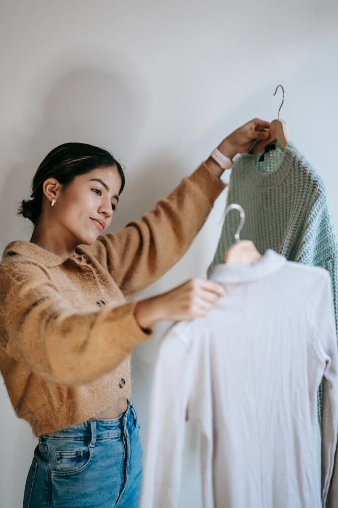 Young woman selecting trendy sweaters indoors, showcasing modern fashion.