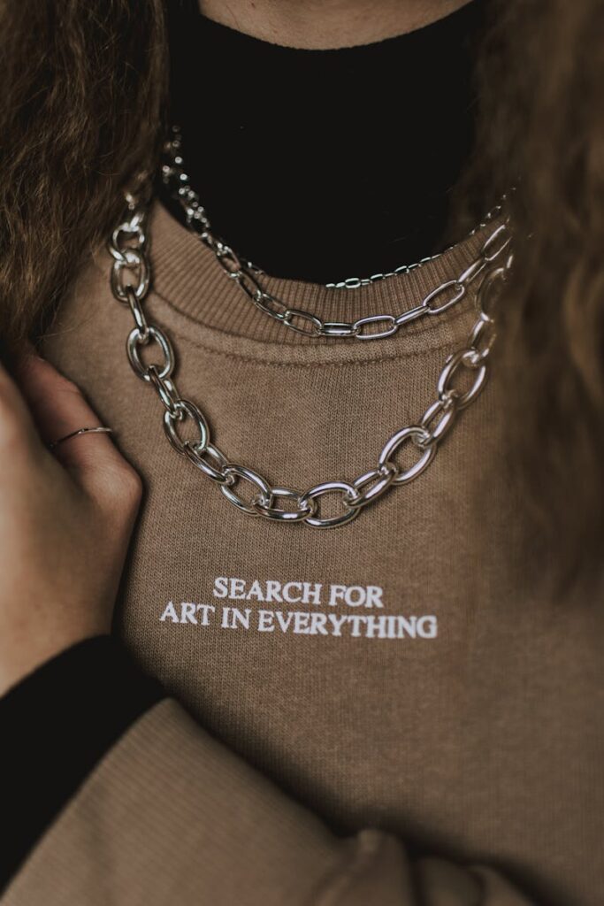 Close-up of a beige sweatshirt with a silver necklace and art slogan.