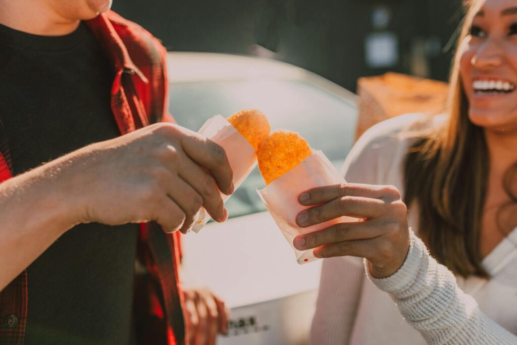 Two friends enjoying hash browns together on a sunny day, creating a cheerful atmosphere.