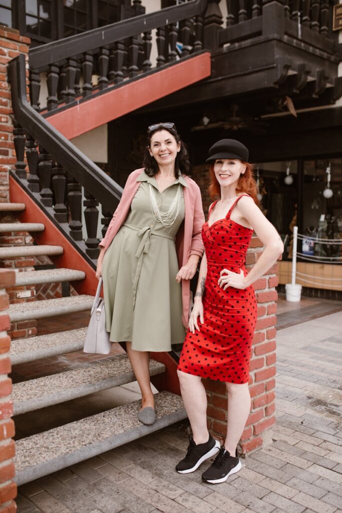 Two stylish women posing on a staircase, showcasing elegant dresses, sunglasses, and accessories.