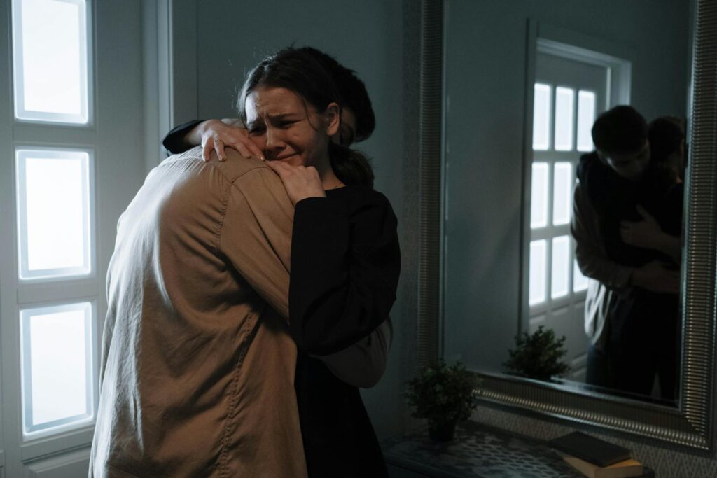 A touching scene of two adults hugging with reflection in mirror, indicating emotional support.