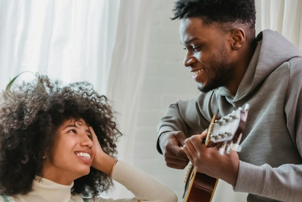 Happy couple bonding over guitar music indoors, creating joyful moments.