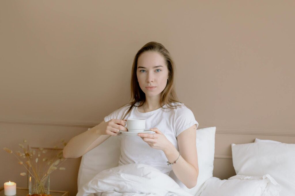 Adult woman relaxing in bed with a morning coffee, creating a peaceful and cozy setting.