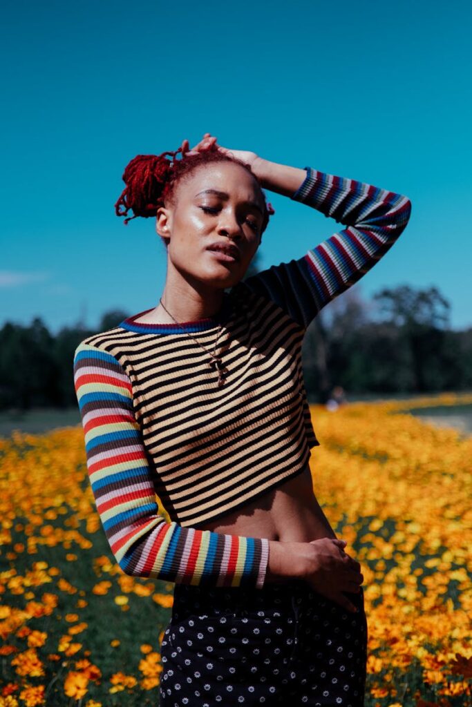 Confident woman with red hair posing in a colorful floral field on a sunny day.