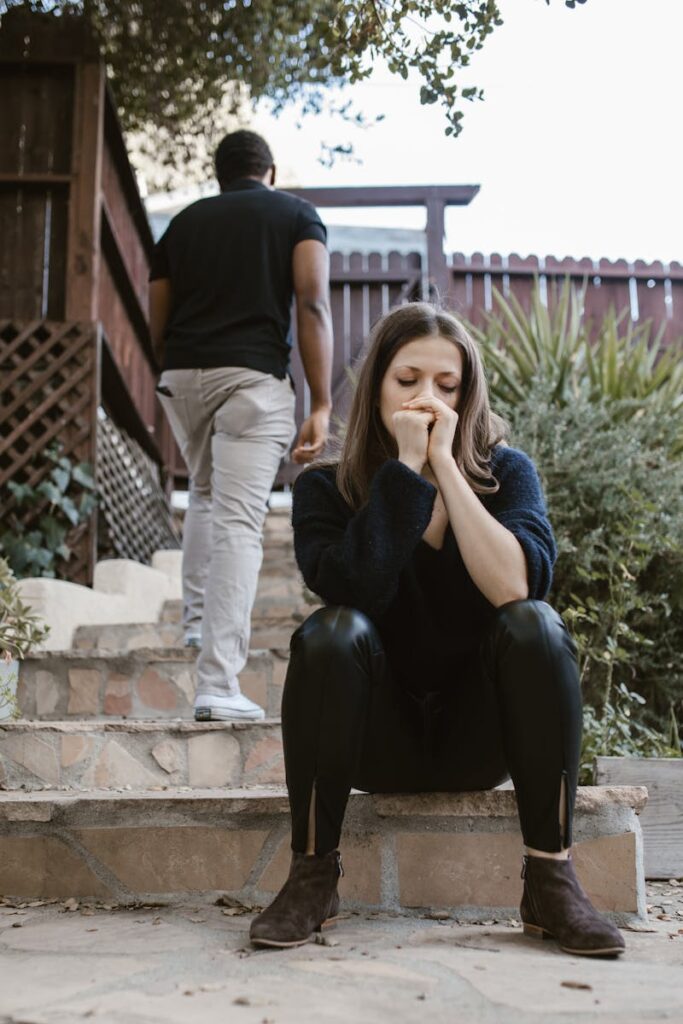 A woman sitting in distress while a man walks away outdoors, capturing emotion and separation.