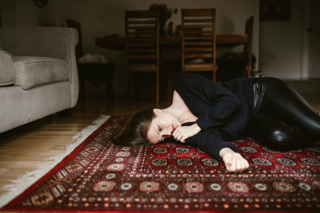 A contemplative woman resting on an intricate oriental rug in a cozy living space.
