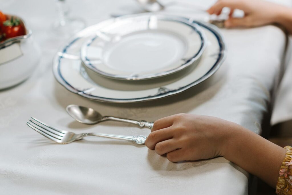 Close-up of a child's hand with elegant tableware on a white tablecloth, creating a refined dining ambiance.