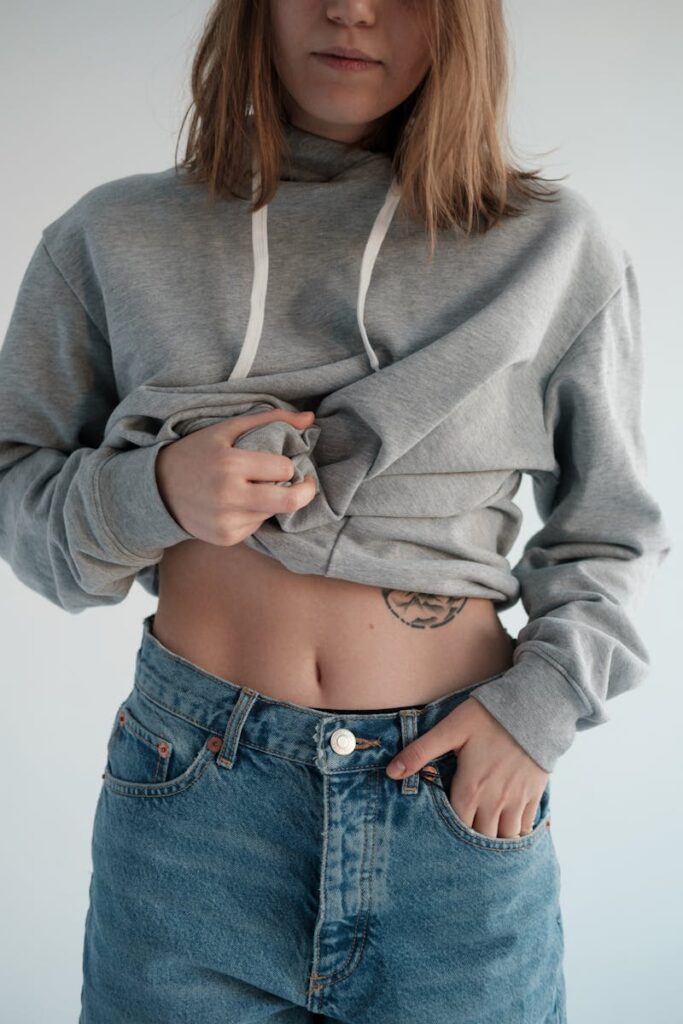 Woman in jeans and hoodie showing tattoo in casual fashion shoot.