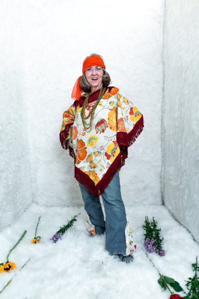 Elegant senior woman in bohemian attire posing joyfully indoors with floral accents.
