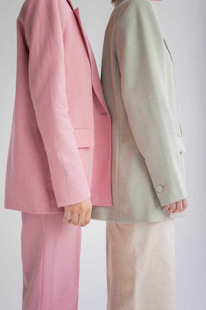 Side view of crop anonymous female models wearing similar trendy suits standing together against gray background