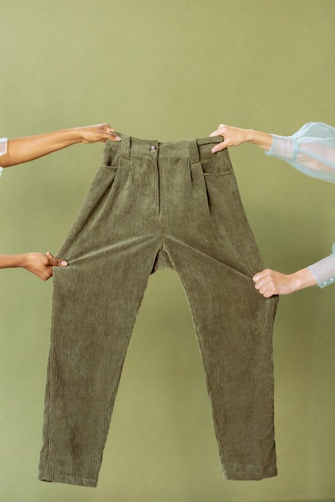 Two people hold green corduroy pants against a matching background.